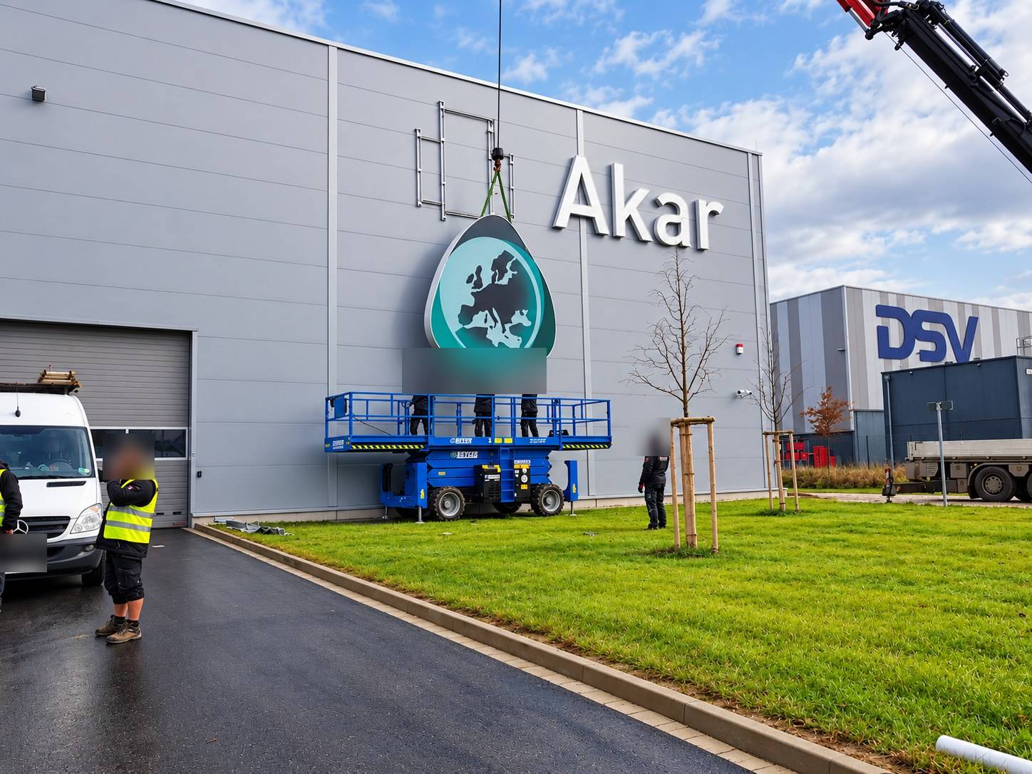 Montage des Akar-Leuchtlogos mit Kran und Hubarbeitsbühne an einer Logistikhalle