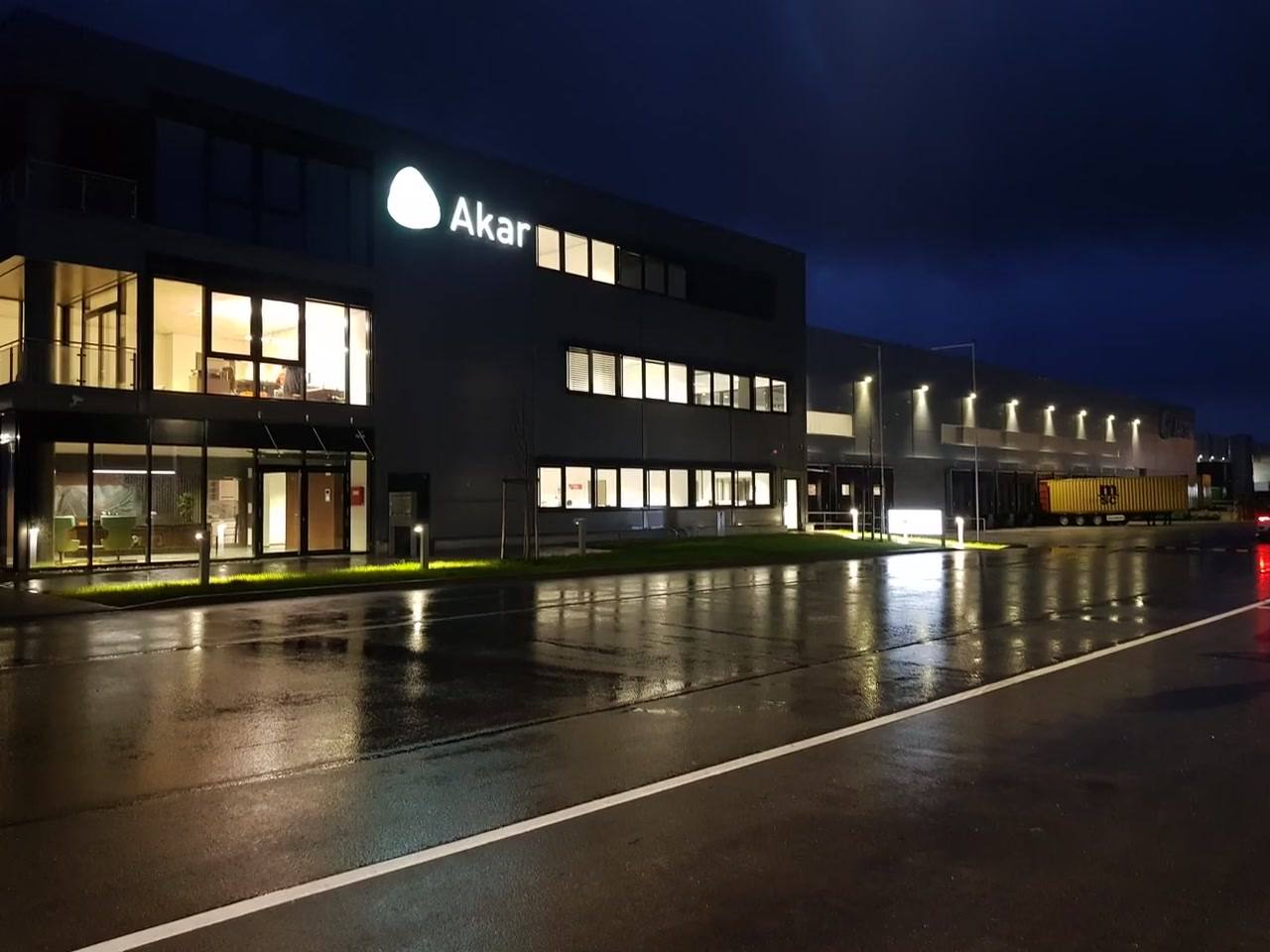 Bürogebäude von Akar bei Nacht mit leuchtendem Logo, nasse Straße