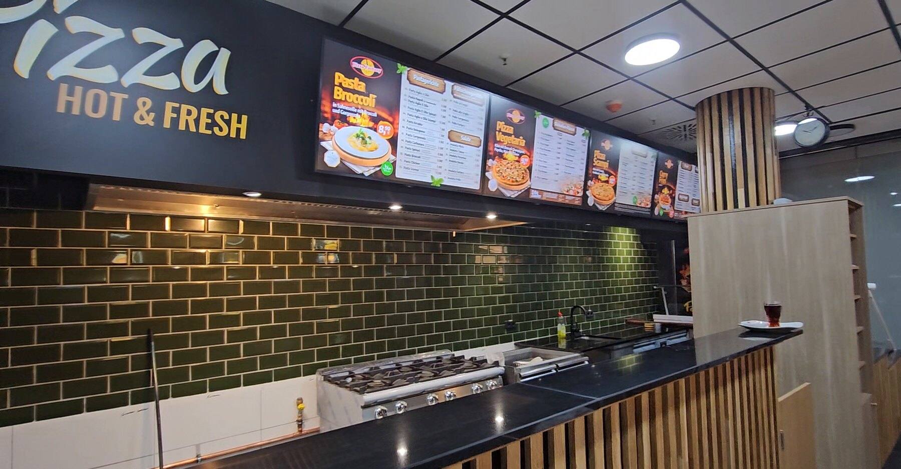 Theke von Pizza Factory mit drei Menübildschirmen über der Küche und Wandgrafik „Pizza hot & fresh“, Inhalte aus WSCREEN